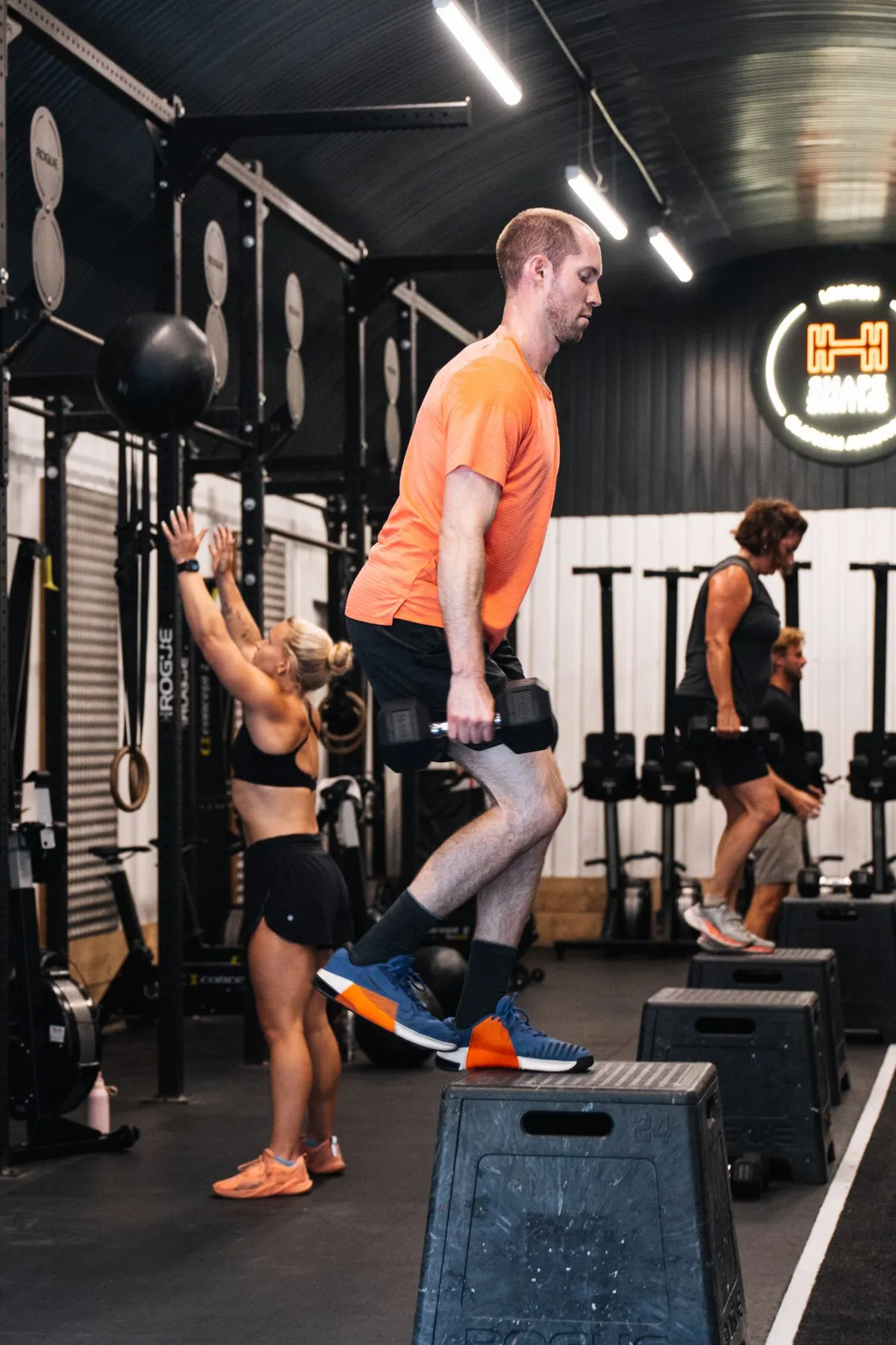 Member stepping up onto a plyo box holding dumbbells in an Engine class at Shapesmiths, Clapham Junction