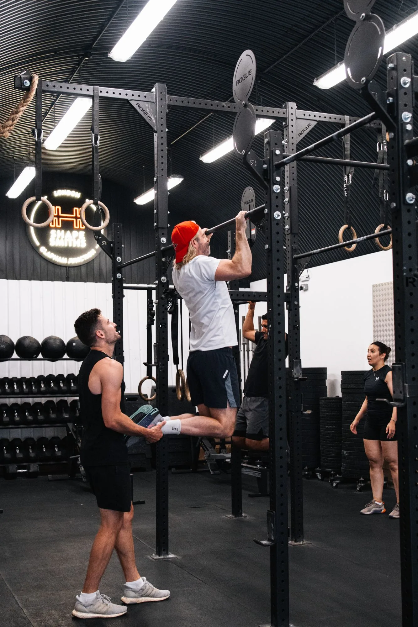 A coach spotting a member's strict pull-up progression on the rig at Shapesmiths, Clapham Junction